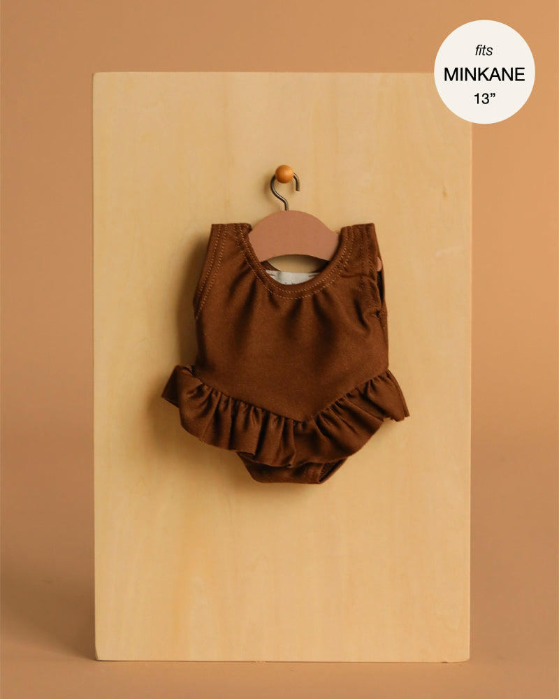 The Maïa Ruffled Leotard in Soft Lycra – Chocolate Brown hangs on a wooden hanger against a beige background, designed to perfectly fit Minikane 13" dolls. "Fits MINIKANE 13''" label shown in the corner.