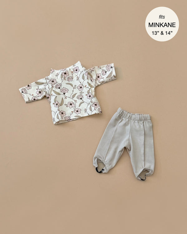 The Natalie Set, featuring a floral long-sleeved shirt with a knit composition and light gray pants, is displayed on a beige background. Text in the corner notes that this hand-washable outfit fits Minikane 13" and 14" dolls.