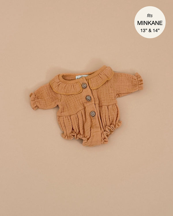 The Leonore Romper, a light brown button-up with ruffled sleeves and collar, is showcased on a beige background. Hand washable and made for Minikane Gordis dolls, it includes a circular label in the top right corner stating "fits 13'' & 14’’.