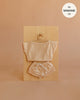 The Mrs. Ertha Doll Clothes - 13″-14″ - Blush Comfy Set, featuring a short-sleeve top and drawstring shorts in a soft beige hue made from organic cotton, is displayed on a wooden hanger against a wooden board. Text in the top right reads “fits Minikane 13” doll clothes.”.