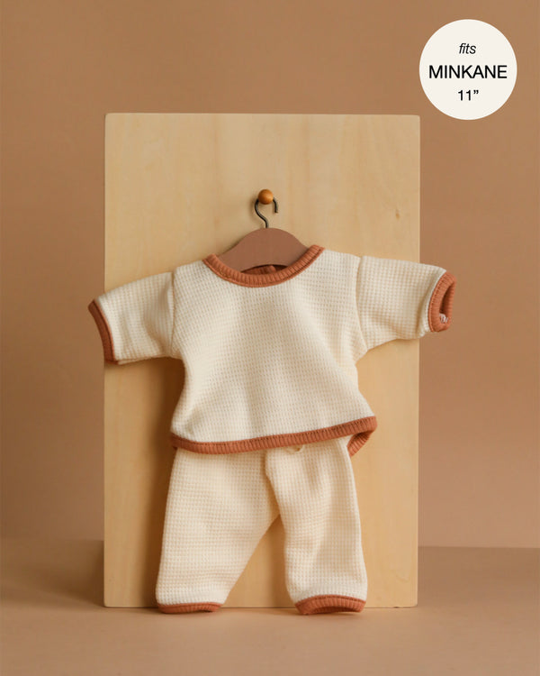 The Minikane 11" Doll Clothing Cocoon Jogger Set in Honeycomb Cotton - Ecru features a cream long-sleeve waffle-knit top and pants with brown trim, displayed on a hanger; label shows "fits MINKANE 11''" in the corner.