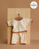 The Minikane 11" Doll Clothing Cocoon Jogger Set in Honeycomb Cotton - Ecru features a cream long-sleeve waffle-knit top and pants with brown trim, displayed on a hanger; label shows "fits MINKANE 11''" in the corner.