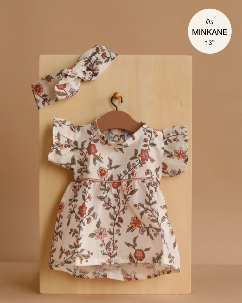 The Minikane 13" Doll Clothing | Daisy Dress & Headband in Cotton - Gisele features a floral dress with flutter sleeves and matching headband, displayed on a wooden hanger. Perfect fit for Minikane dolls sized 13 inches.