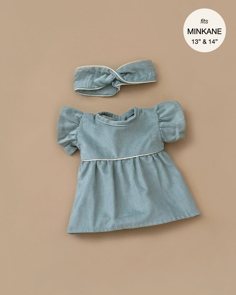 A sage green Daisy dress with puffed sleeves and matching headband on a beige background, designed in France, suitable for Minikane dolls 13" & 14".