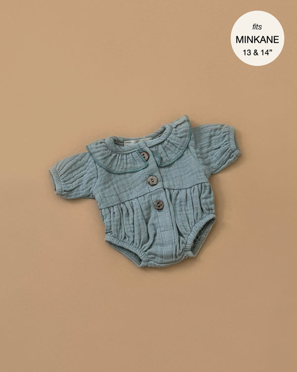 A small, textured Leonore ruffled jumpsuit in Baltic Green with short sleeves and a Peter Pan collar, adorned with three buttons down the front. Specially designed for Minikane dolls, it is displayed on a beige background. A circular label in the corner states "fits Minikane 13 & 14".