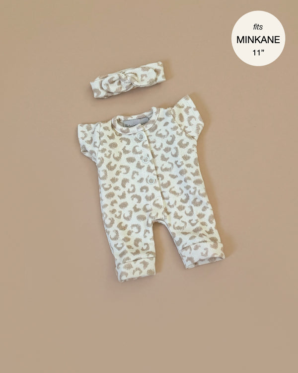 The Minikane 11" Doll Clothing | Lili Jumpsuit in Féline Fleece features a soft, cotton, beige and white leopard print outfit with short sleeves and pants. It comes with a matching headband, perfectly designed for an 11" Minikane doll against a plain beige background.