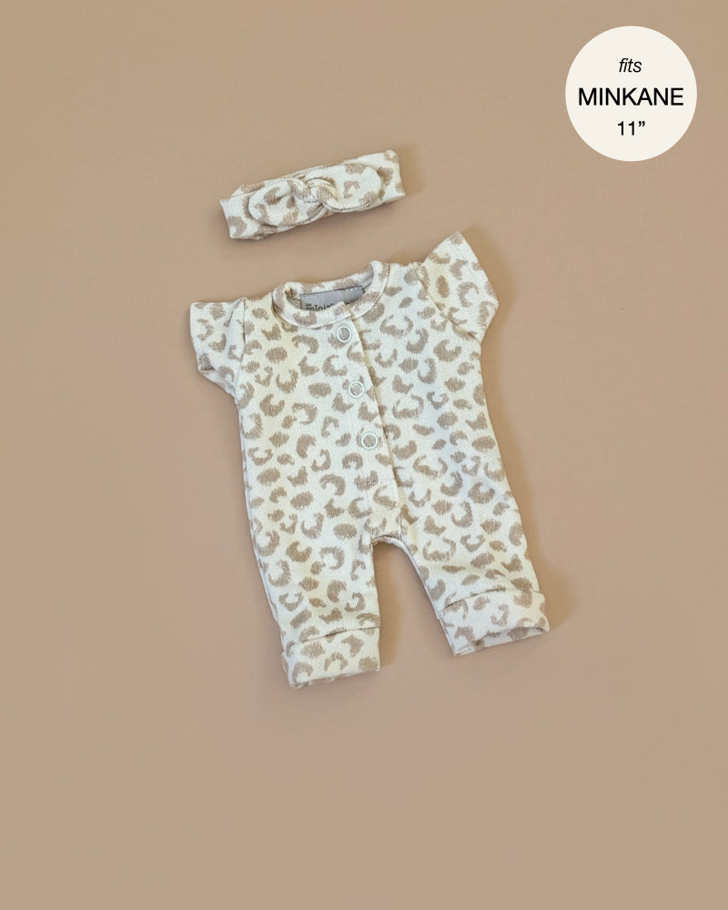 The Minikane 11" Doll Clothing | Lili Jumpsuit in Féline Fleece features a soft, cotton, beige and white leopard print outfit with short sleeves and pants. It comes with a matching headband, perfectly designed for an 11" Minikane doll against a plain beige background.