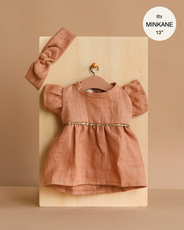 The Minikane Doll Clothing set features a rust-toned Daisy Dress with puffed sleeves and a matching headband in washed linen (Hazelnut). Fits 13-inch Minikane dolls—perfect for refreshing your doll’s wardrobe!.