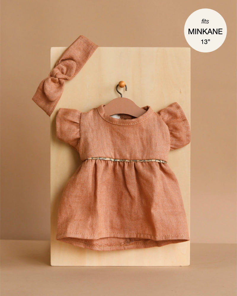 The Minikane Doll Clothing set features a rust-toned Daisy Dress with puffed sleeves and a matching headband in washed linen (Hazelnut). Fits 13-inch Minikane dolls—perfect for refreshing your doll’s wardrobe!.