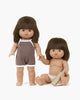Two Minikane Chléa dolls with short brown hair feature similar expressions. One stands in a brown sleeveless outfit, while the other sits in a diaper holding a comb. Both exude a subtle vanilla scent for added charm.