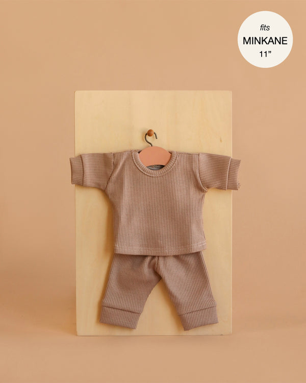The Minikane 11" Doll Clothing | Morgan Pajama in Ribbed Cotton - Mocha features a small ribbed mocha long-sleeve shirt and matching pants for 11-inch dolls, displayed on a wooden board. Text in a white circle states "fits Minikane dolls.