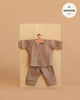 The Minikane 11" Doll Clothing | Morgan Pajama in Ribbed Cotton - Mocha features a small ribbed mocha long-sleeve shirt and matching pants for 11-inch dolls, displayed on a wooden board. Text in a white circle states "fits Minikane dolls.