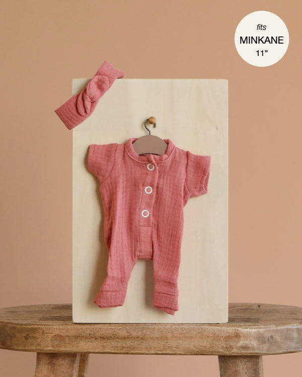 The Minikane 11" Doll Clothing | Lili Jumpsuit & Headband in Cotton Gauze - Marsala is shown on a wooden hanger and board atop a stool. Short-sleeved, button-up, with matching headband. Text reads "fits MINIKANE 11''" in the top right corner.