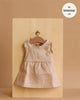 The Minikane 13" Doll Sleeveless Faustine Dress in Washed Linen - Nude, featuring a gathered skirt, is shown on a wooden hanger against a board. Text reads “fits 13 inch doll.” A quality addition to your doll clothing collection.