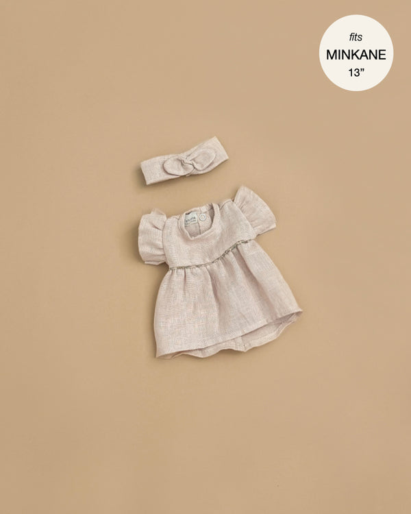 The Minikane Doll Clothing | Daisy Dress & Headband in Washed Linen - Nude features a light beige puff-sleeve dress and matching headband, shown on a tan background. Circular label: fits Minikane dolls & 13 inch dolls.