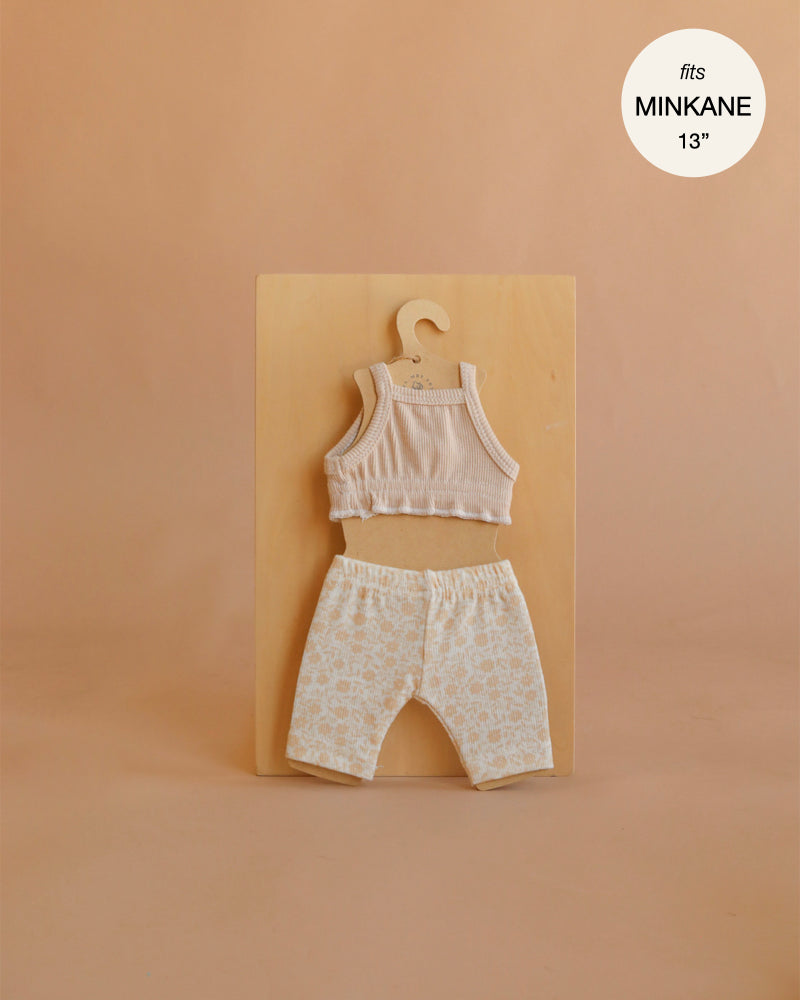 A set of Mrs. Ertha Doll Clothes—Bouquet Silhouette Leggings Set for 13″-14″ dolls—is displayed on a wooden board against a neutral background. Featuring a sleeveless knit top and patterned leggings made from organic cotton, these handmade doll clothes are perfectly tailored, with a “fits Minikane 13” label shown in the top right corner.