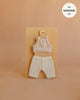 A set of Mrs. Ertha Doll Clothes—Bouquet Silhouette Leggings Set for 13″-14″ dolls—is displayed on a wooden board against a neutral background. Featuring a sleeveless knit top and patterned leggings made from organic cotton, these handmade doll clothes are perfectly tailored, with a “fits Minikane 13” label shown in the top right corner.