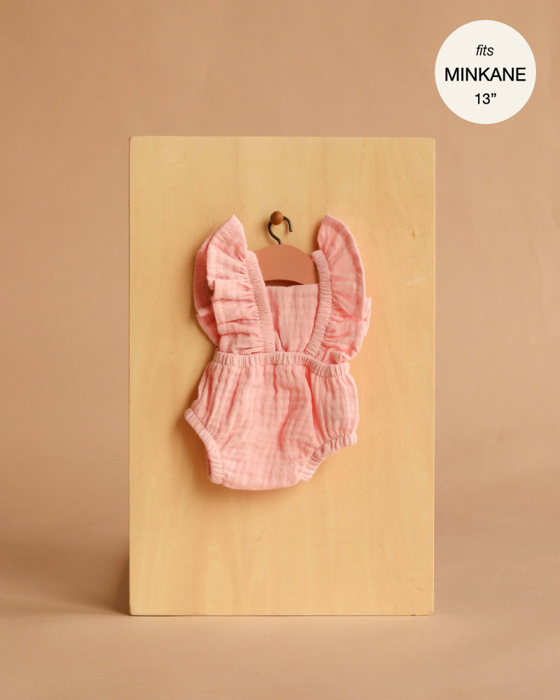 The Lou Retro Romper in Cotton Gauze - Strawberry for Minikane 13" dolls is shown on a small wooden hanger against a light wood board, with a label noting it fits 13" dolls—perfect for dressing up your favorite Minikane doll.