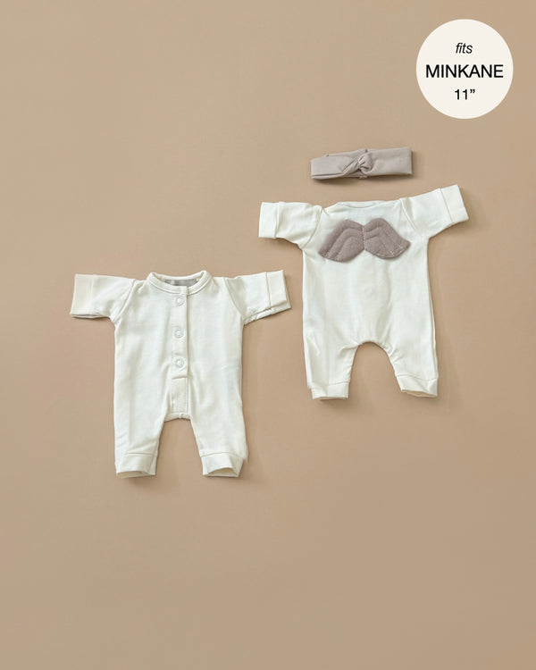 The "Little Angel" Linen Jersey outfits, specially designed for Minikane 11" babies, feature button-down fronts and charming wing designs on the back. Both outfits are a soft white color, each beautifully matched with a coordinating cream headband placed above. A text bubble confirms these are perfect fits for Minikane 11" dolls.