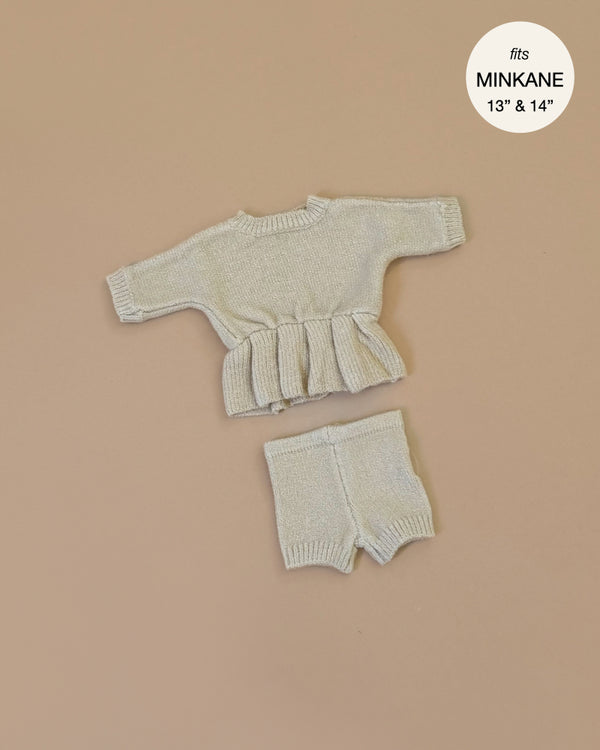 The Minikane Doll Clothing Félicie Set in Cream Knit includes a small beige long-sleeve peplum top and matching shorts, designed for 13" & 14" dolls, exuding charm and snug comfort.