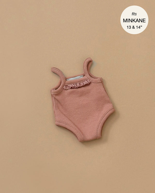 A ribbed knit jumpsuit in brown sugar lies against a beige background, featuring frilled trim around the neckline. Perfectly tailored for Minikane Gordis dolls, a circular label in the top right corner reads "fits MINKANE 13 & 14".