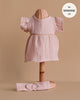 The Minikane Doll Clothing Daisy Dress & Headband in Cotton Gauze - Orchid Pink is a light pink, short-sleeved set for 13" Minikane dolls and also fits as 14" doll clothes, shown on a wicker mannequin stand.