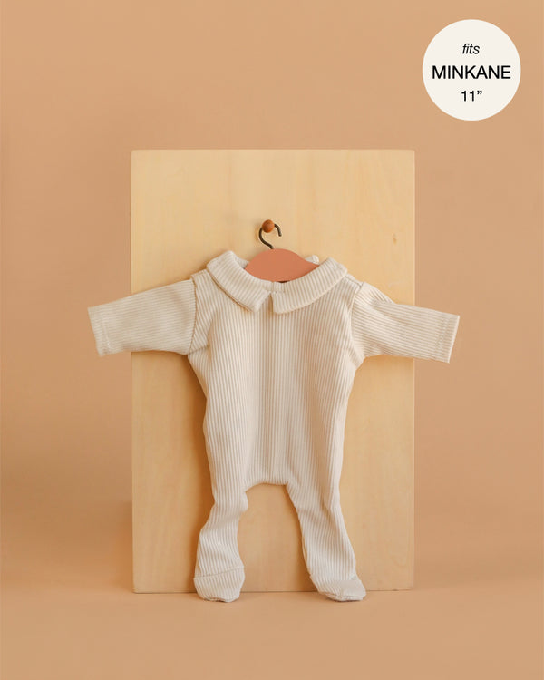 A cream-colored, long-sleeve ribbed knit "Sleep Well Corentin" onesie for Minikane 11" dolls is shown on a hanger against a light wooden board. Made in France.