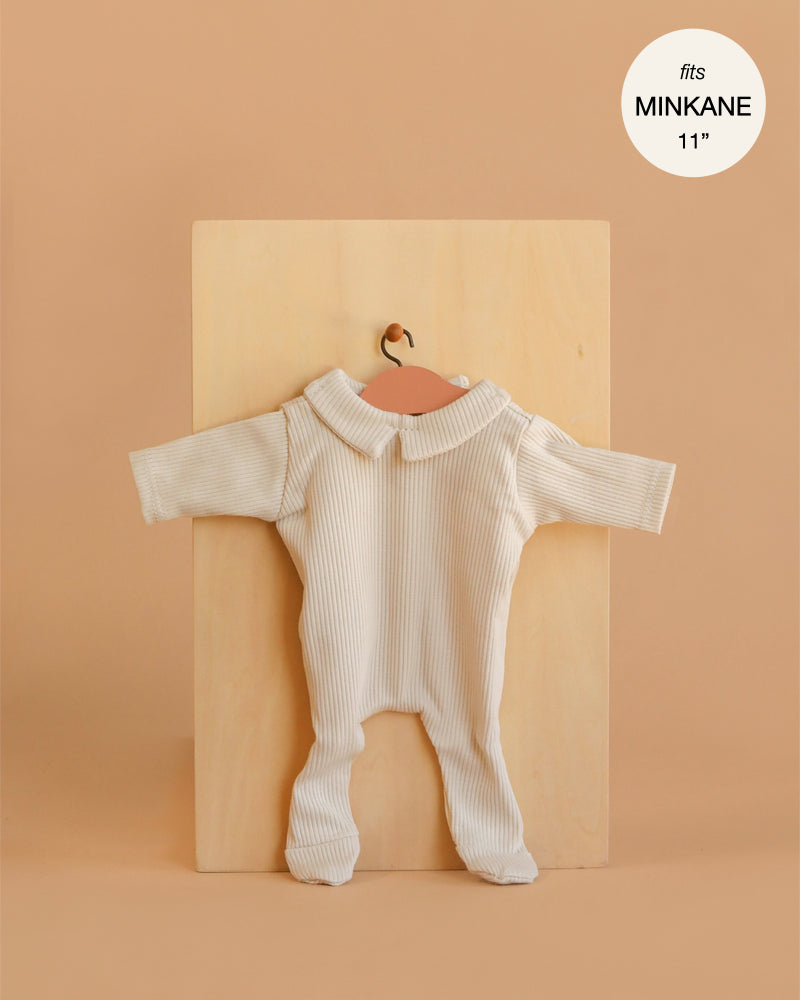 A cream-colored, long-sleeve ribbed knit "Sleep Well Corentin" onesie for Minikane 11" dolls is shown on a hanger against a light wooden board. Made in France.