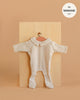 A cream-colored, long-sleeve ribbed knit "Sleep Well Corentin" onesie for Minikane 11" dolls is shown on a hanger against a light wooden board. Made in France.