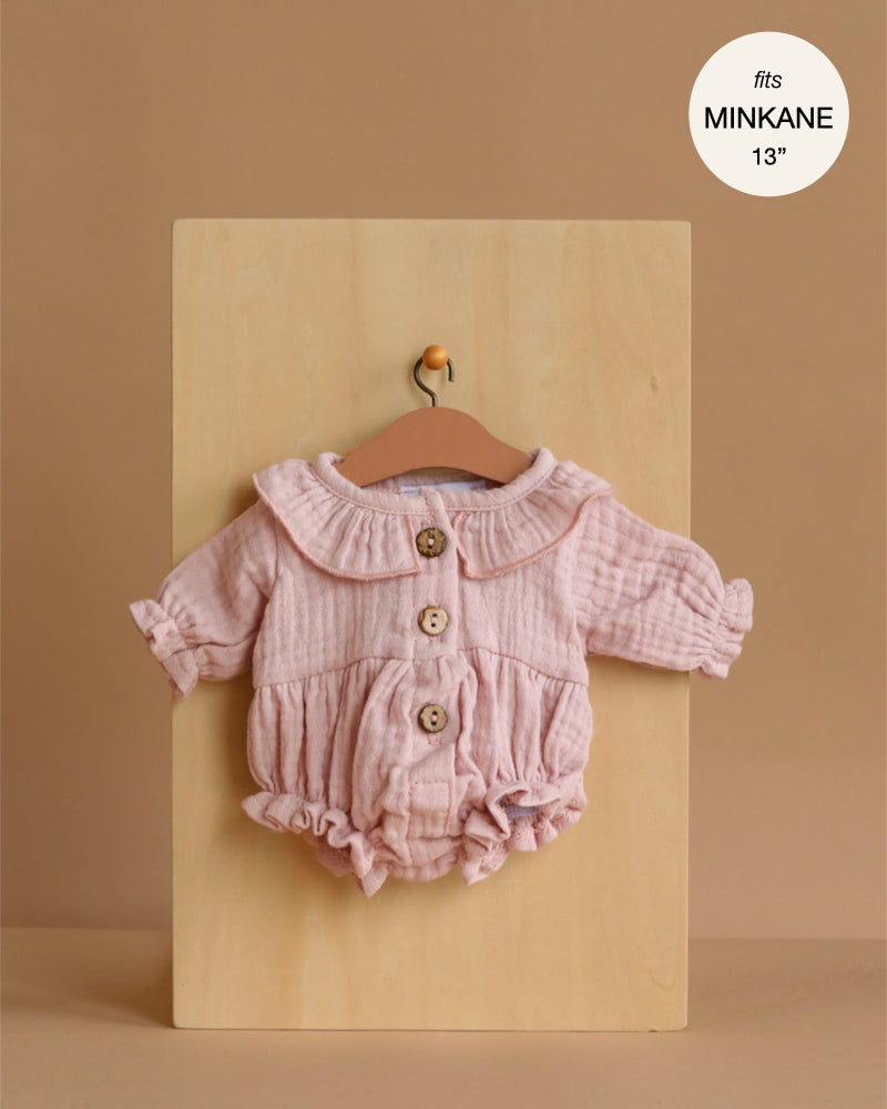 The Minikane Doll Clothing | Leonore Ruffled Romper in Cotton Gauze - Orchid Pink is a light pink, long-sleeve romper with wooden buttons and a ruffled collar, designed to fit Minikane or other 13" dolls. "Fits MINIKANE 13” shown in the corner.