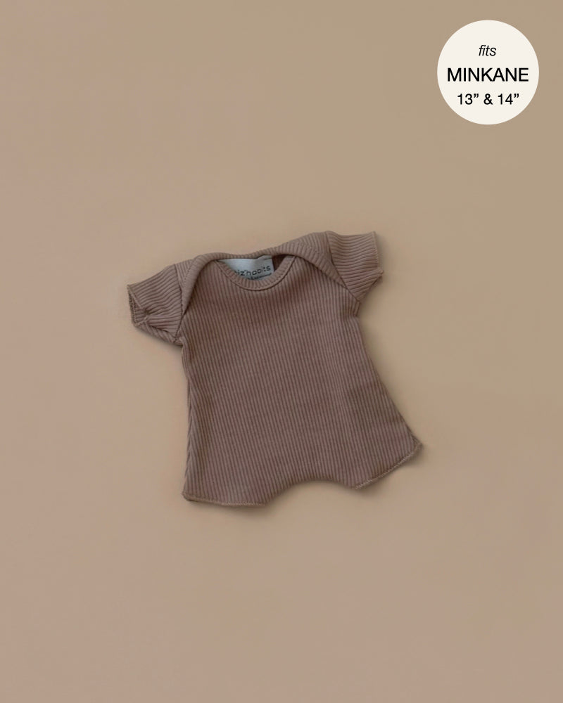 The Minikane 11" Doll Clothing, Cocoa Ribbed Body Shorty—a charming, French-made brown T-shirt crafted from cotton knit—fits 13" and 14" Minikane dolls perfectly and is displayed on a beige background.