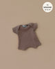 The Minikane 11" Doll Clothing, Cocoa Ribbed Body Shorty—a charming, French-made brown T-shirt crafted from cotton knit—fits 13" and 14" Minikane dolls perfectly and is displayed on a beige background.