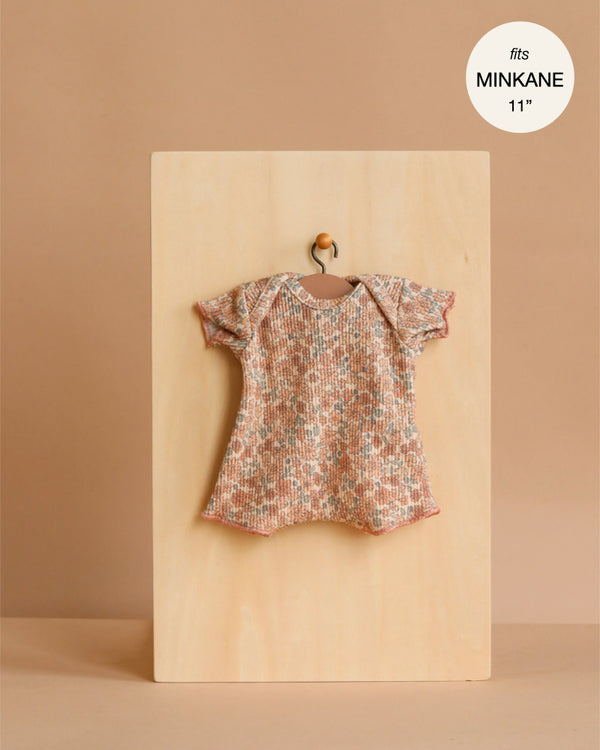A Minikane 11" Doll Clothing Shorty Bodysuit in Ribbed Knit - Cocoa Flowers hangs on a tiny wooden hanger against a plain board, labeled as fitting 11-inch Minikane dolls.