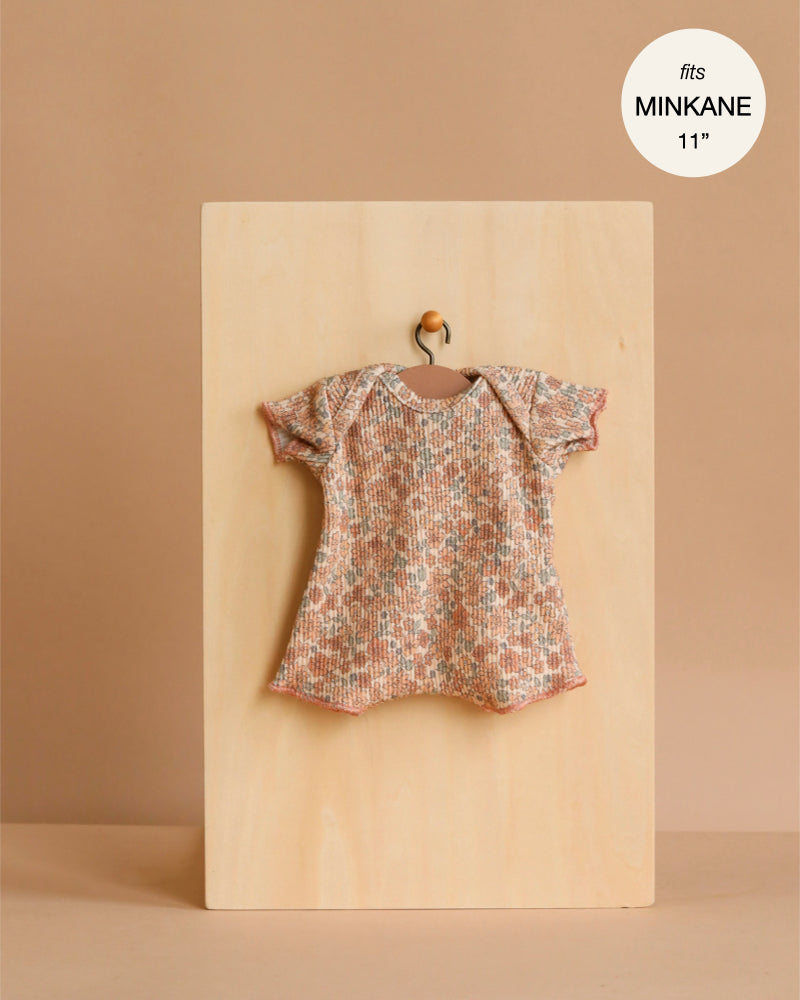A Minikane 11" Doll Clothing Shorty Bodysuit in Ribbed Knit - Cocoa Flowers hangs on a tiny wooden hanger against a plain board, labeled as fitting 11-inch Minikane dolls.