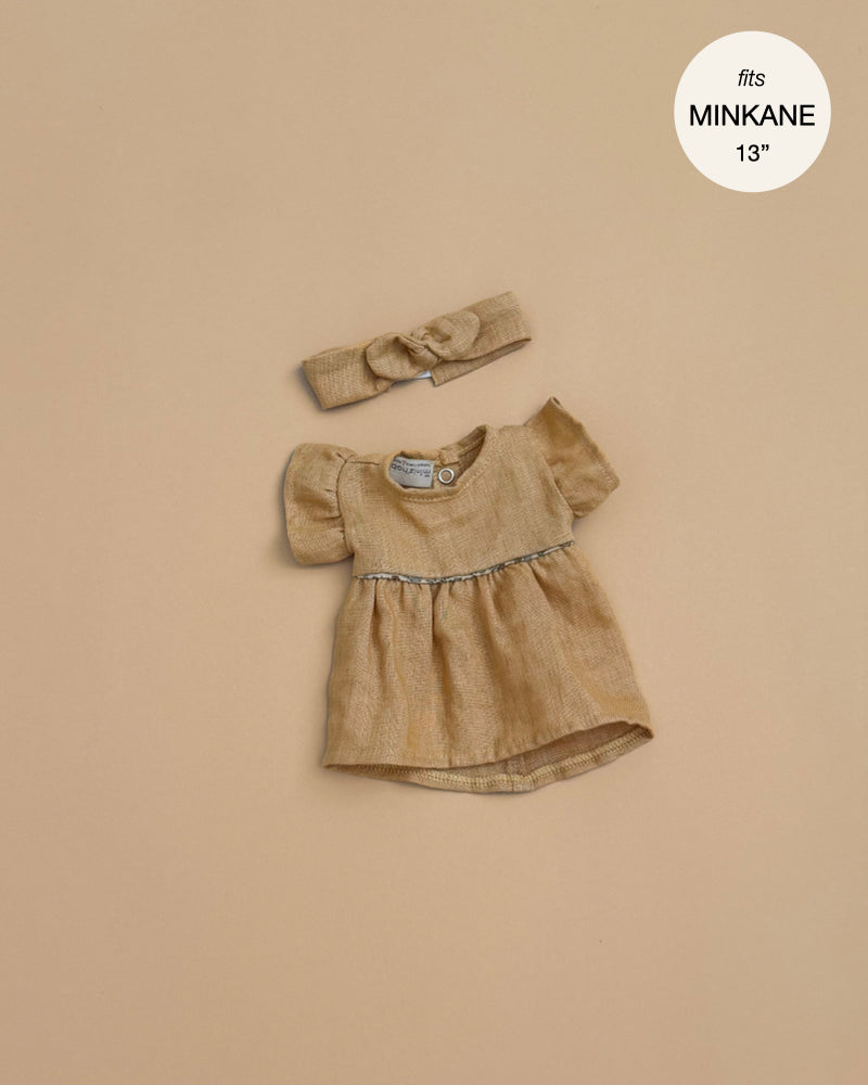 The Minikane Doll Clothing Daisy Dress & Headband in Washed Linen - Oatmeal features a small beige dress with puffed sleeves and gathered waist, plus a matching bow headband, displayed on beige. Fits Minikane and 13-inch dolls.
