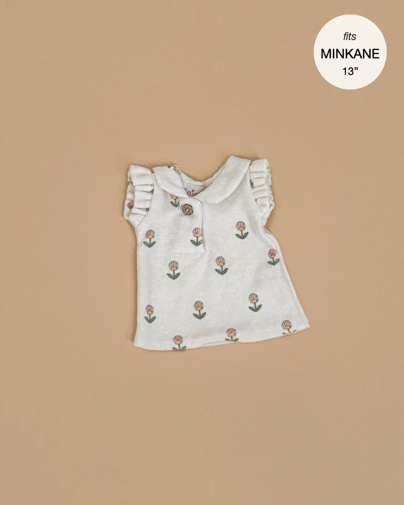 The Minikane Doll Clothing | Emile & Ida, Emilia Dress in Soft Terrycloth - Flower is a small sleeveless white dress with ruffled shoulders and brown button, designed in France for Minikane 13" and 14" dolls. Features tiny tulip flowers.