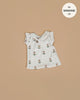 The Minikane Doll Clothing | Emile & Ida, Emilia Dress in Soft Terrycloth - Flower is a small sleeveless white dress with ruffled shoulders and brown button, designed in France for Minikane 13" and 14" dolls. Features tiny tulip flowers.