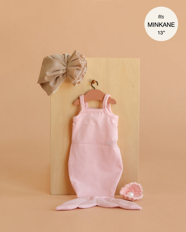 The Minikane 13" Doll Clothing | Mermaid Costume & Pink Pearl Seashell Set includes a pink mermaid tail dress on a wooden hanger, a taupe headband, and a pink crocheted accessory. Text reads: "fits MINIKANE 13.