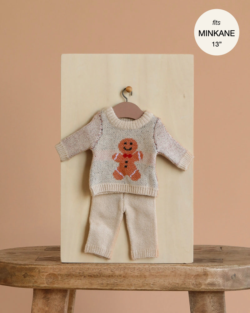 The Minikane 13" Doll Clothing | Christmas Gingerbread Two-Piece Knit Set features a cream knit sweater with a gingerbread man and matching pants—perfect clothes and accessories for 13 inch Minikane dolls.