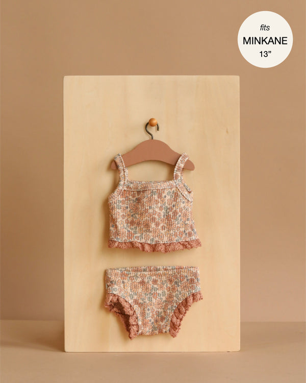 The Minikane 13" Doll Clothing | Les P'tits Basiques, 2-Piece Set in Jersey - Cocoa Flowers features a floral top and matching shorts with ruffled edges, displayed on a wooden hanger. A circle label reads "fits MINIKANE 13”".