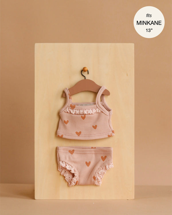 The Minikane 13" Doll Clothing | Les P'tits Basiques 2-Piece Set in Ribbed Cotton - Pink Hearts includes a tank top and matching lace-trim bloomers for Gordis dolls. Displayed on a wooden hanger, made in France. Fits MINIKANE 13".