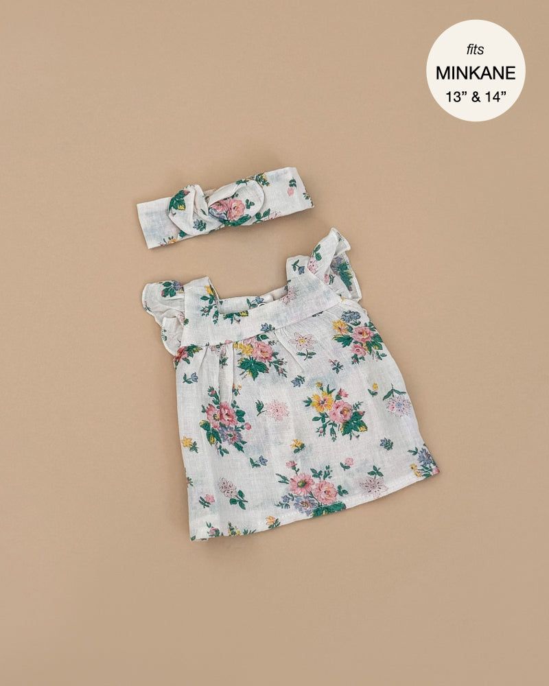The Ida Pink Spring Dress & Headband from Emile & Ida offers a floral sleeveless dress with ruffled straps on beige, designed for 13" and 14" Minikane dolls. Adorned in pink and yellow flowers, it's hand washable and includes a matching headband. Designed in France.