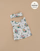 The Ida Pink Spring Dress & Headband from Emile & Ida offers a floral sleeveless dress with ruffled straps on beige, designed for 13" and 14" Minikane dolls. Adorned in pink and yellow flowers, it's hand washable and includes a matching headband. Designed in France.