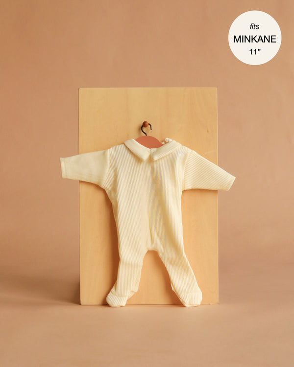 The Minikane 11" Doll Clothing | Sleep Well Corentin Onesie in ribbed yellow knit features a collar and covered feet. Displayed on a hanger against a wooden board, it's designed to fit Minikane Dolls 11".