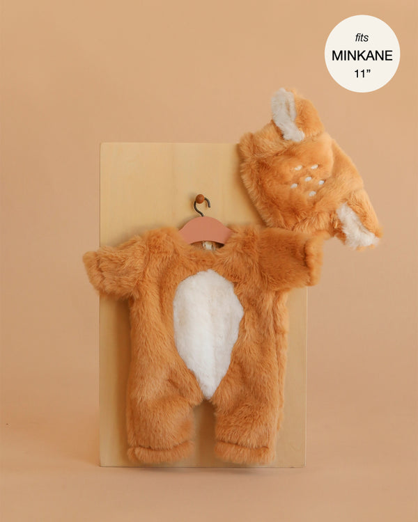 The Minikane 11" Doll Clothing | Bambi Costume—a fuzzy brown and white outfit with a hat featuring animal ears and white spots—hangs on a small hanger, perfect for 11" dolls like Minikane. Label reads "fits MINKANE 11".