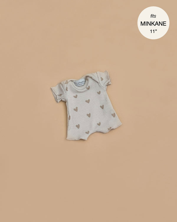 This ribbed cotton bodysuit for Minikane 11" dolls features short sleeves and a beige heart pattern. Shown on a plain tan background, the text "fits MINIKANE 11" appears in the top right corner.