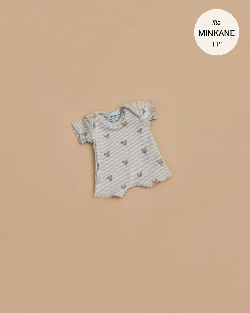 This ribbed cotton bodysuit for Minikane 11" dolls features short sleeves and a beige heart pattern. Shown on a plain tan background, the text "fits MINIKANE 11" appears in the top right corner.