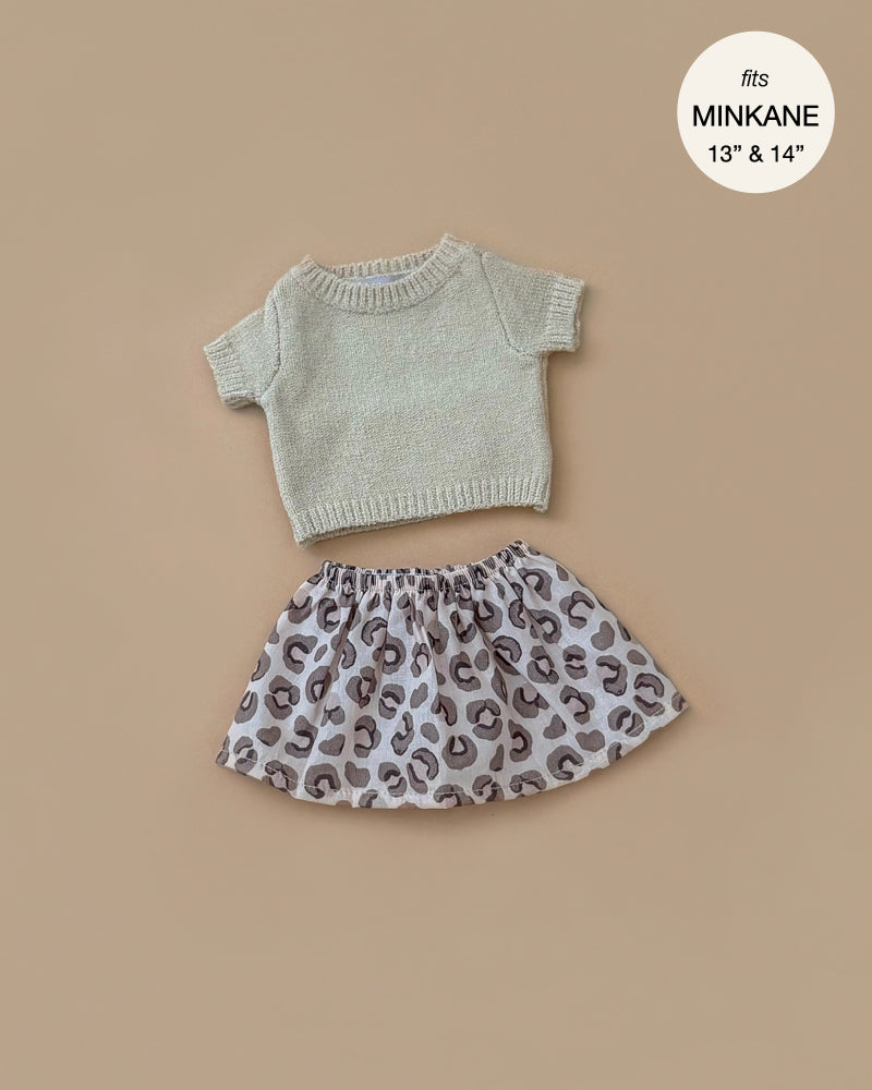 The Minikane Doll Clothing | Paula Cream Sweater & Réjane Skirt Set features a small cream knit sweater and leopard print skirt for 13" and 14" Minikane dolls, elegantly displayed on a beige background and hand washable.