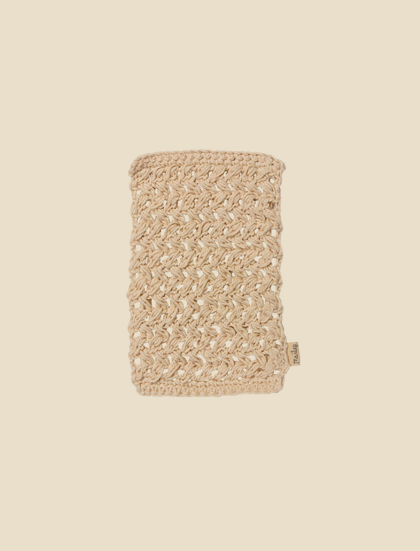 A hand-knit beige wool blanket with a cable knit pattern is neatly folded and positioned vertically against a plain cream background, displaying a small tag attached to the bottom right corner reminiscent of the meticulous attention to detail seen in the Maileg Bath Mat.