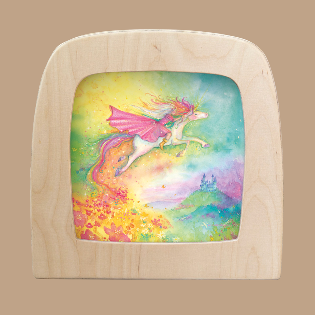 A Unicorn Silhouette for Toverlux Lamp features a flying unicorn with pink wings above a rainbow landscape with flowers and a distant castle, capturing the magic of Toverlux in a charming silhouette display.